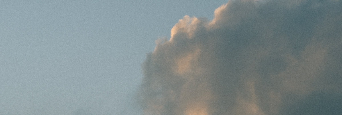 A scenic photograph of a dramatic cloud formation against a pale blue sky, with warm golden light catching the cloud's edges.